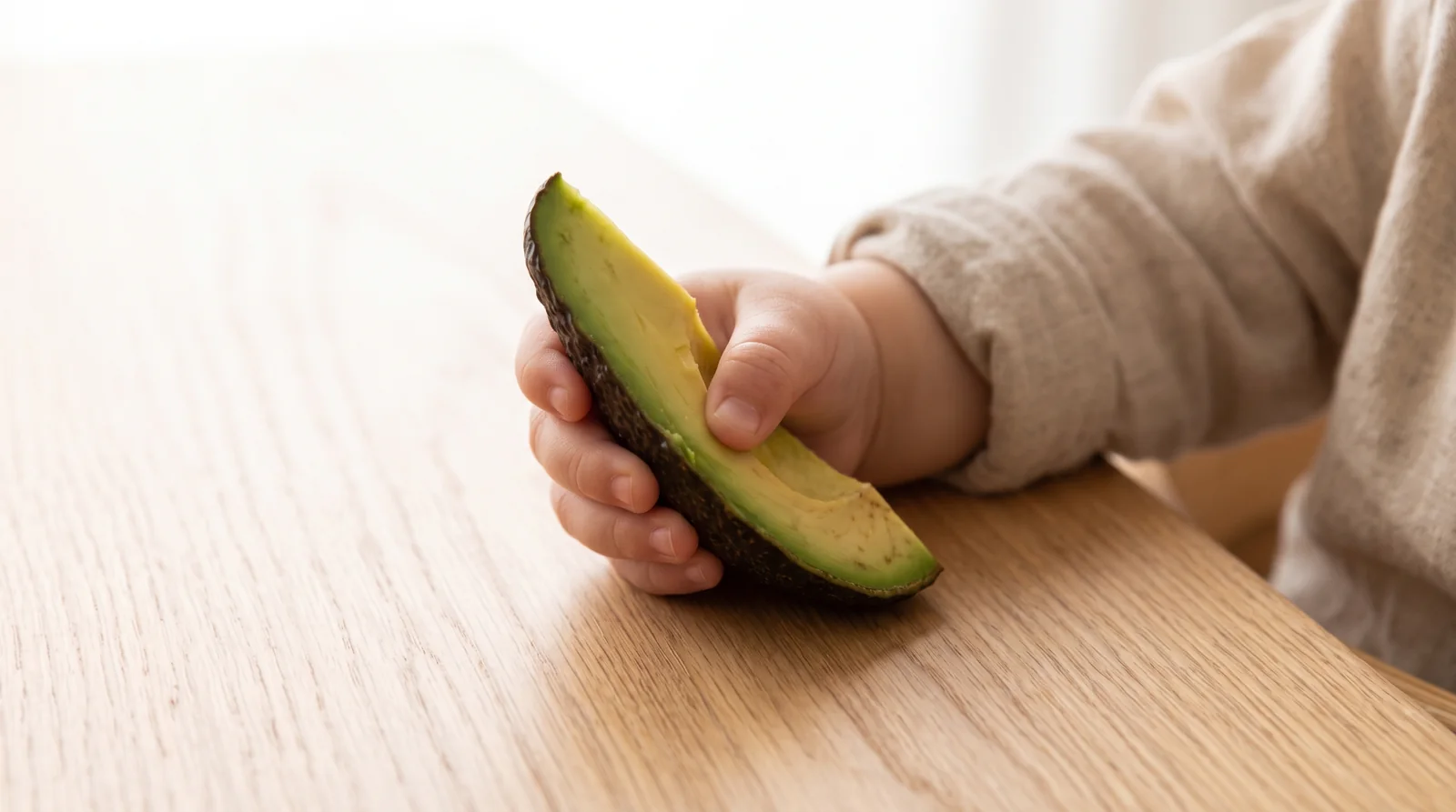 Mano de un bebé sujetando un gajo de aguacate